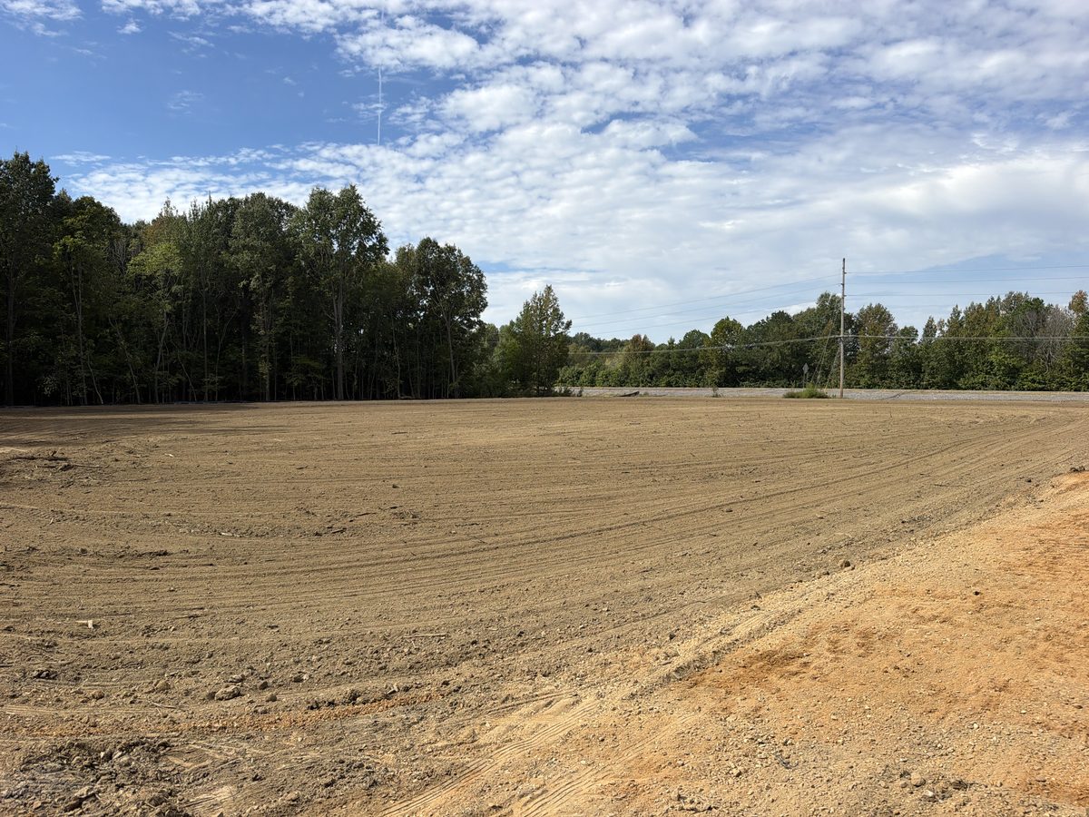 Same site cleared, stumps removed and graded flat into a buildable dirt pad ready for construction
