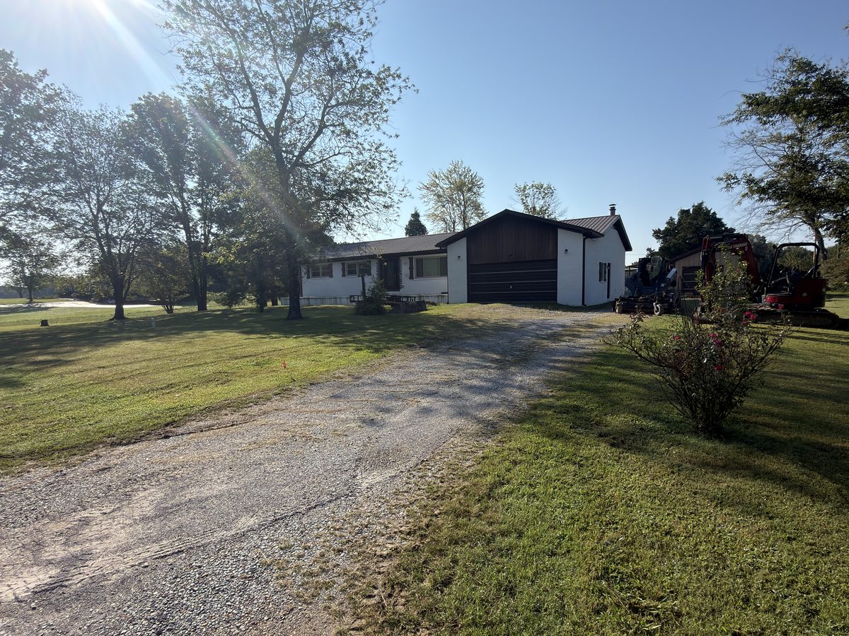 Narrow gravel driveway with thin rock and grass encroaching from both edges, before repair, Western Kentucky